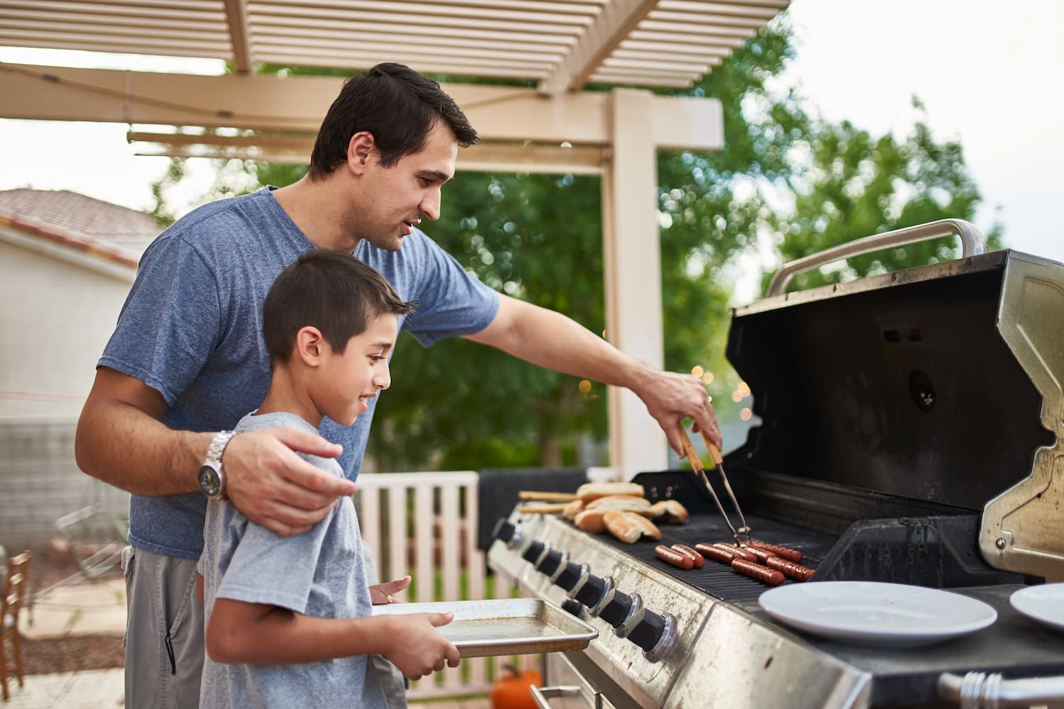 father teaching son how to grill on backyard covered porch