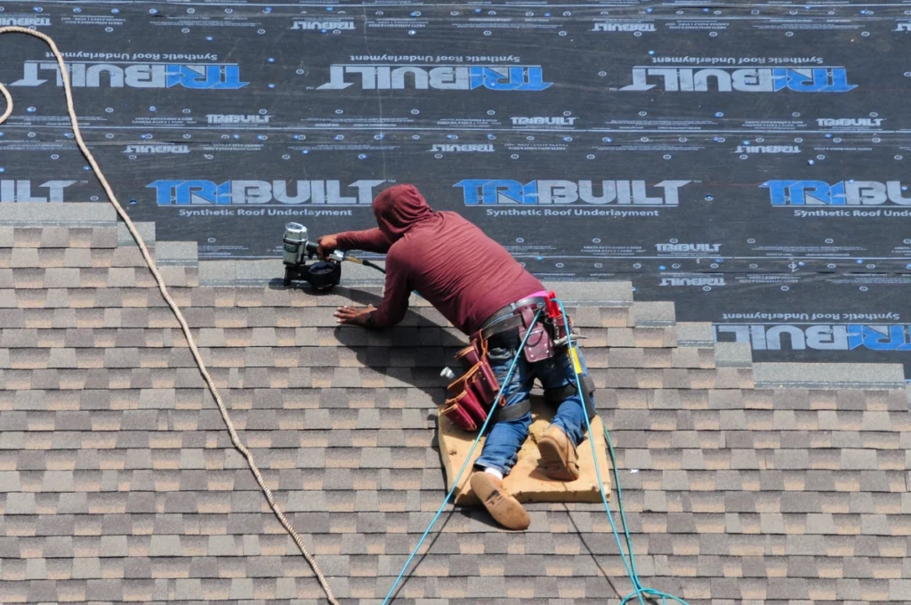 worker nailing the asphalt shingles on Synthetic roof underlayment