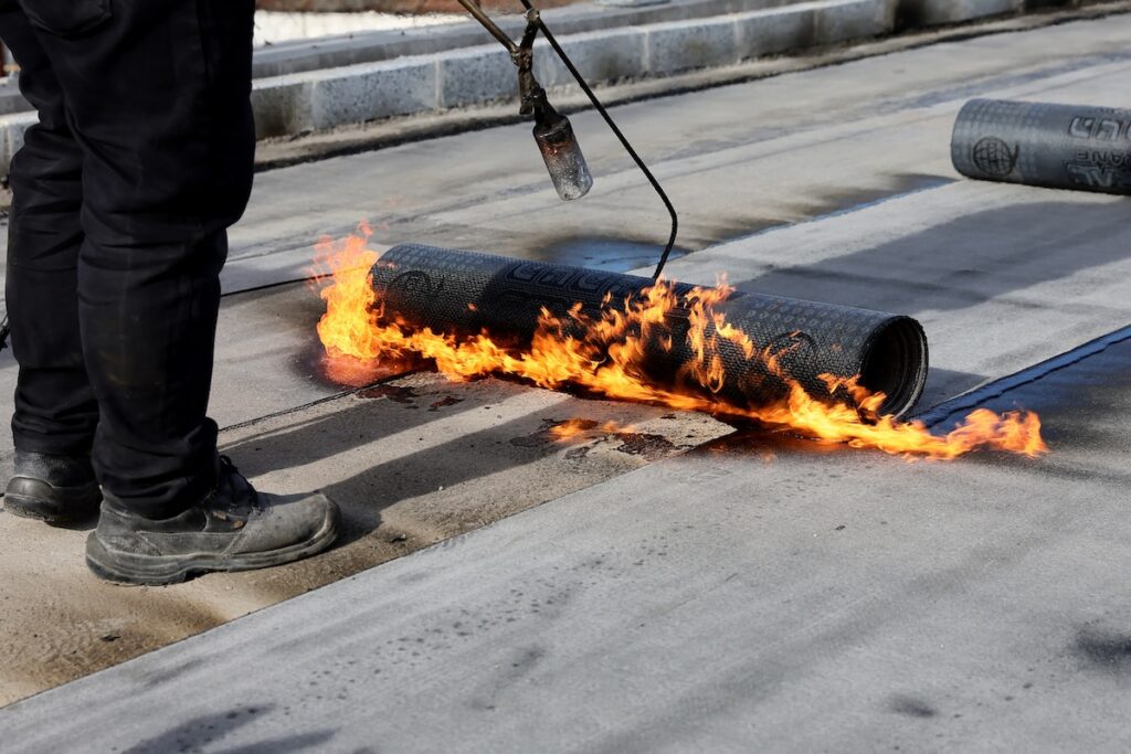 Professional construction workers using a blowtorch to glue modified bitumen roll sheet over roof
