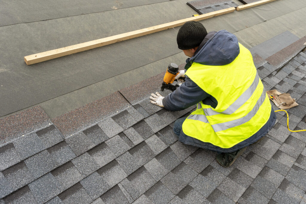 a worker installing asphalt shingles on roof