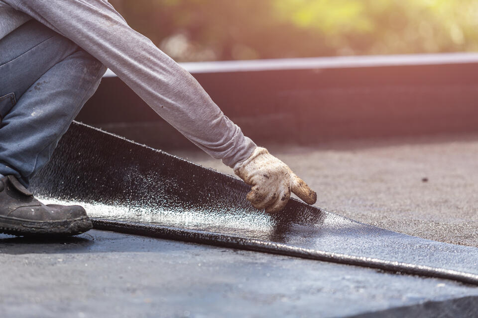flat roof repair-close up of man in gloves installing new section of black flat roofing materials