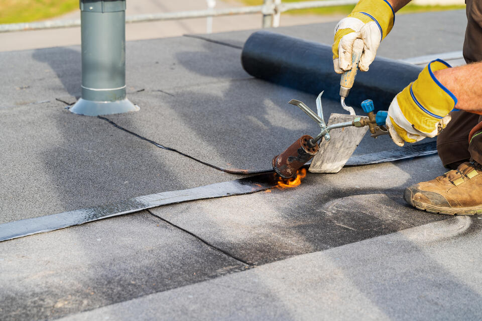 flat roof repair-man in yellow gloves using torch to patch section of flat roof