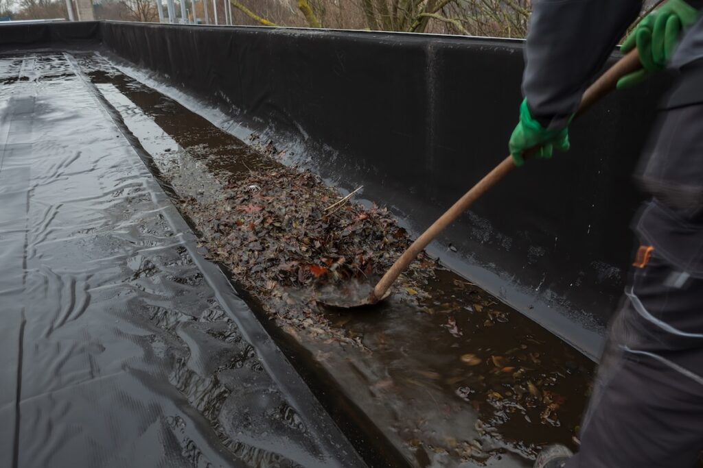 The gutter of a flat roof is full of debris from the trees such as leaves and branches,