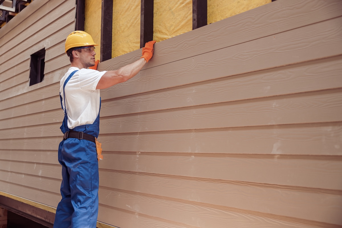 construction worker wearing safety helmet and work overalls while installing wood siding