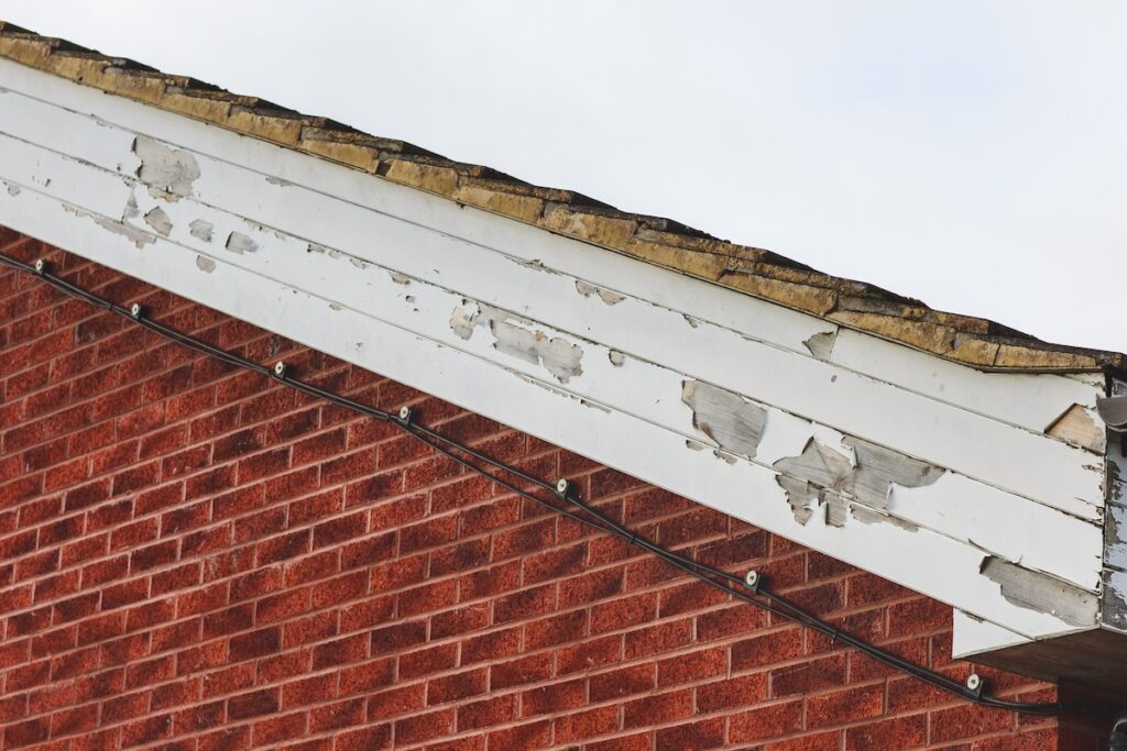 flaking paint and cracked fascia board on brick house