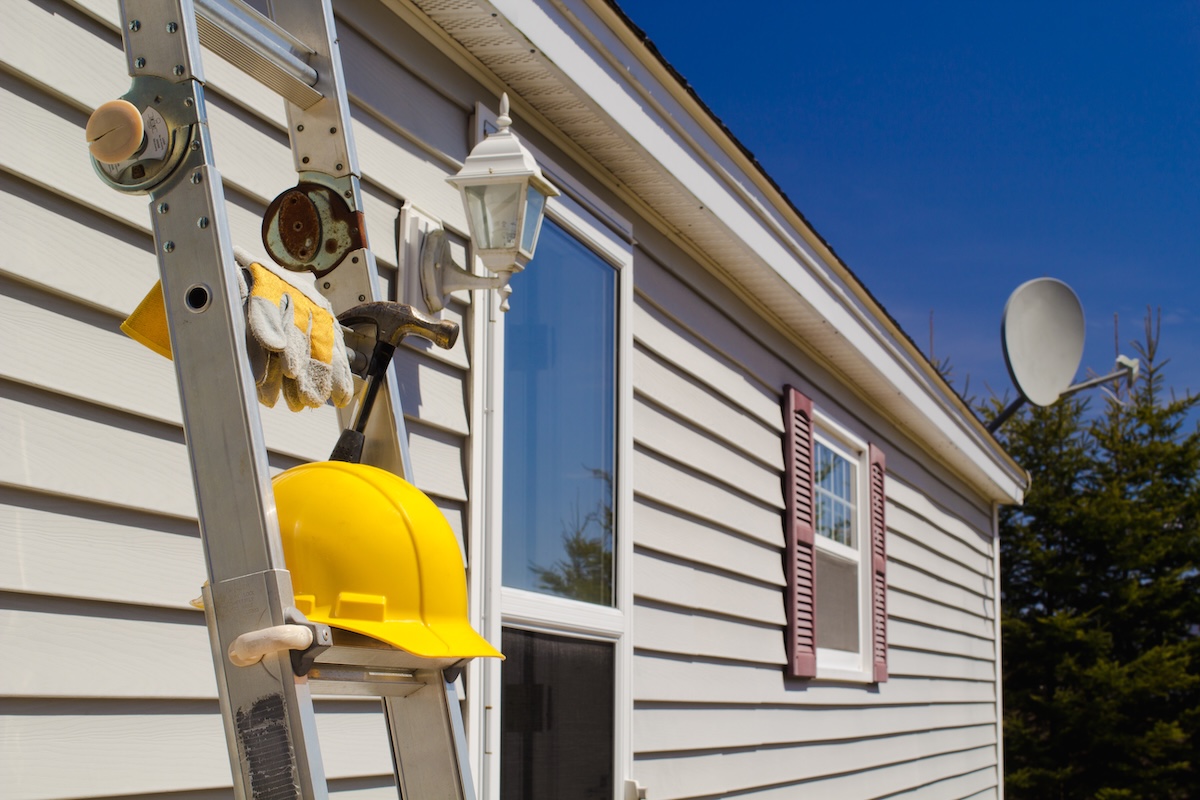 Yellow hard hat, work gloves and hammer on ladder with house