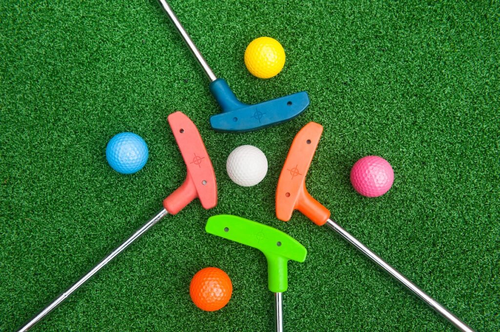 Four colorful golf putters with golf balls on synthetic grass