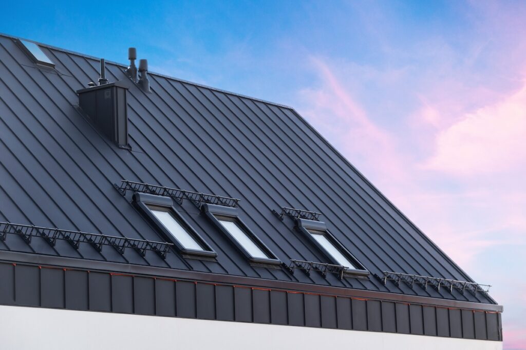 House with metal roof and skylight windows with sunset sky in background