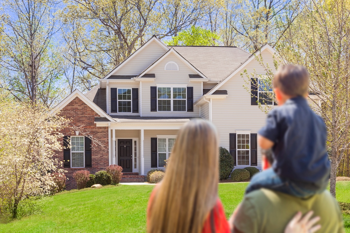 Young family looking at the exterior of a house with child on the father's shoulders