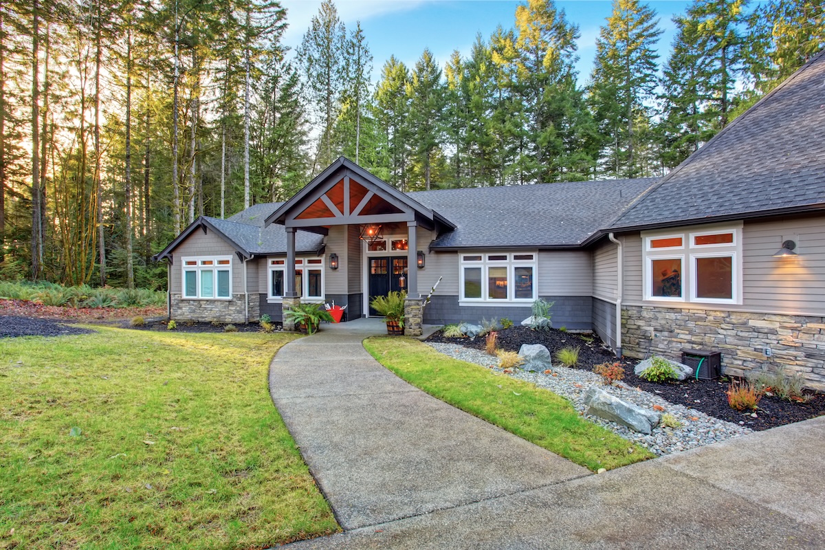 Beautiful large house with driveway, and garage. Tanish gray siding with landscaping around edge of house