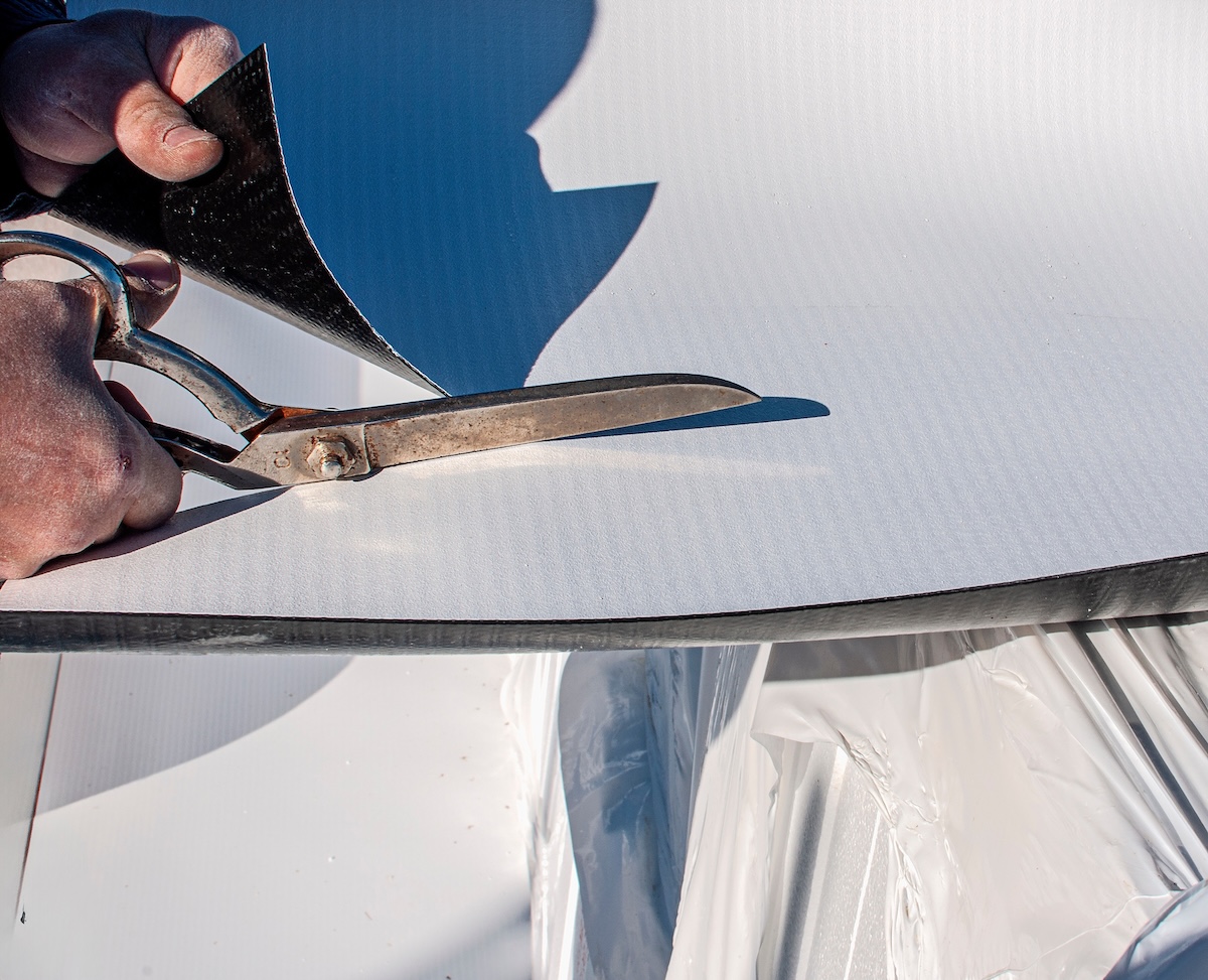 Construction worker cuts with large scissors a TPO polyolefin sheet to be applied for waterproofing a terrace of a commercial building
