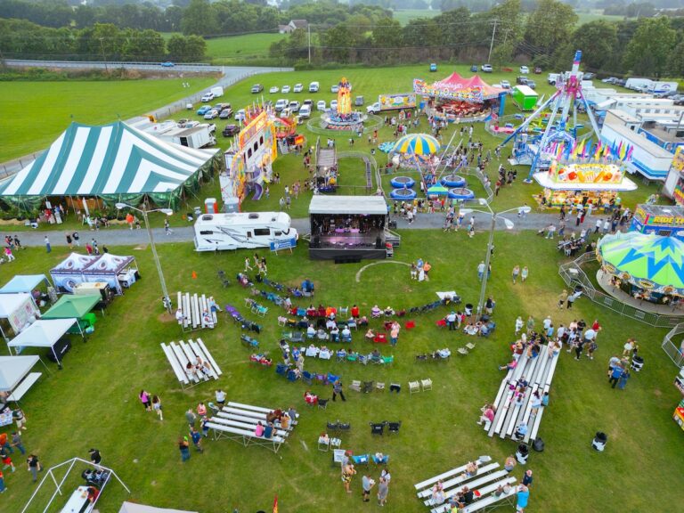 Aerial drone view of a county fair, dirt track, and a parking lot with cars.