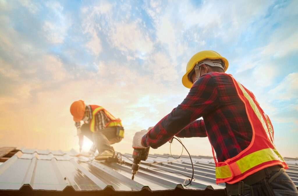 Roofer worker in protective uniform wear gloves, using electric screw drill installing iron roof or metal sheet on top of the new roof