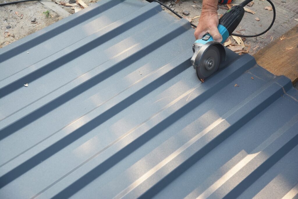 A roofer is cutting with a power angle grinder a corrugated metal sheet