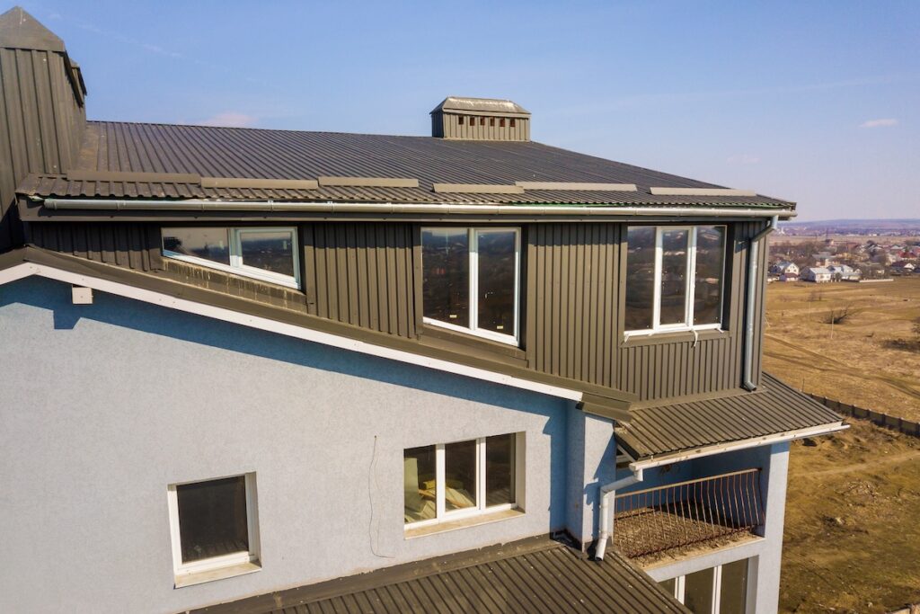 Aerial view of attic annex room exterior with plastic windows, roof and walls covered with brown metal decorative siding planks, new gutter system