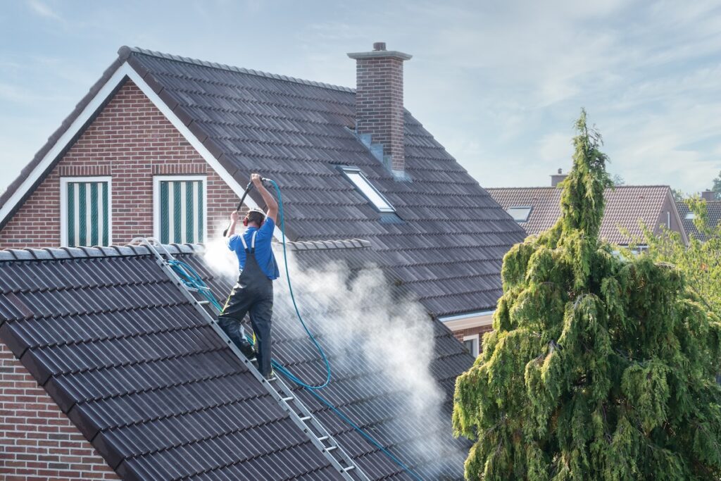 Cleaner with pressure washer at roof of house cleaning the roof tiles, removing moss and weed