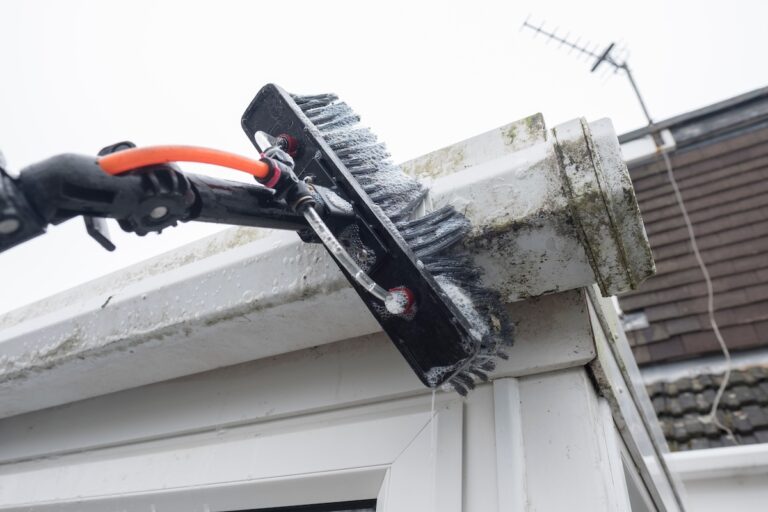 A brush cleaning dirty clogged white plastic pvc gutters and drain pipes with mossy green mold