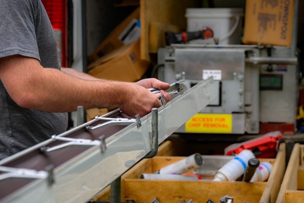 Hands of a Technician in the process of installing custom-made gutters on our home in Windsor in Upstate NY. The skilled hands of a craftsman preparing gutters for installation