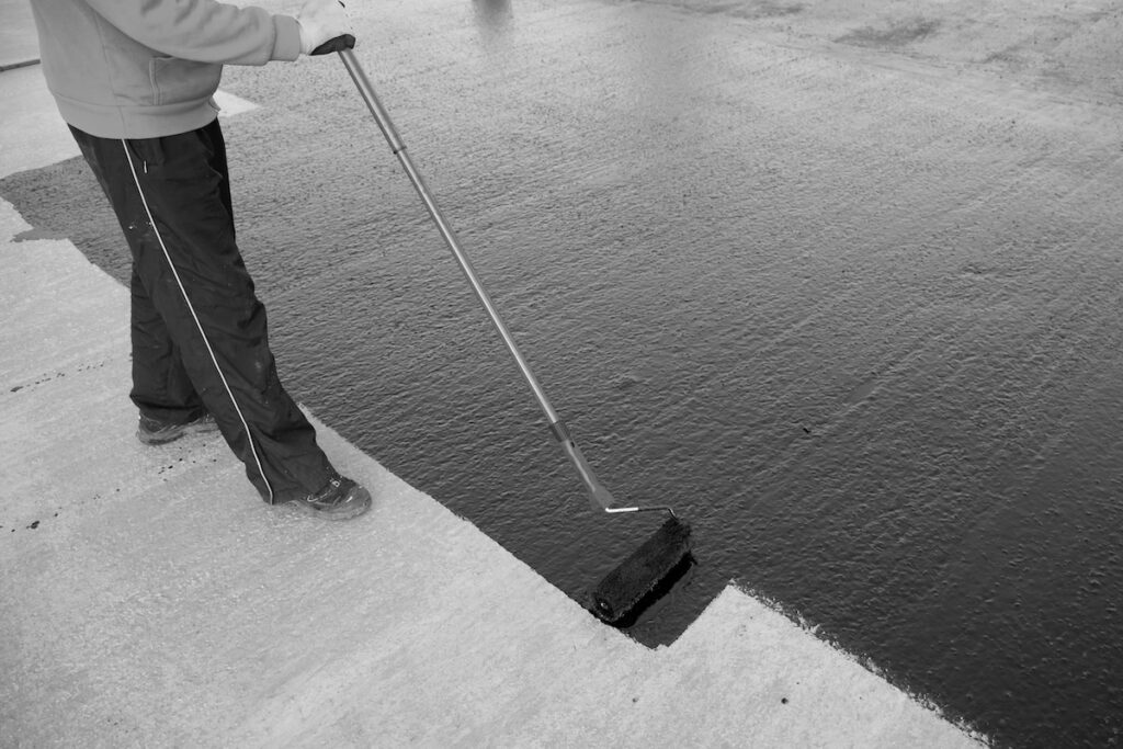 Waterproofing coating. Worker applies bitumen mastic on the foundation. Roofer cover the rooftop polymer modified bitumen waterproofing primer, with a roller brush.