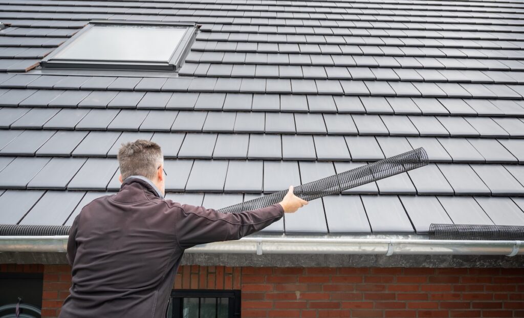 Man puts a gutter mesh to the rain gutter to protect the gutter from leaves.
