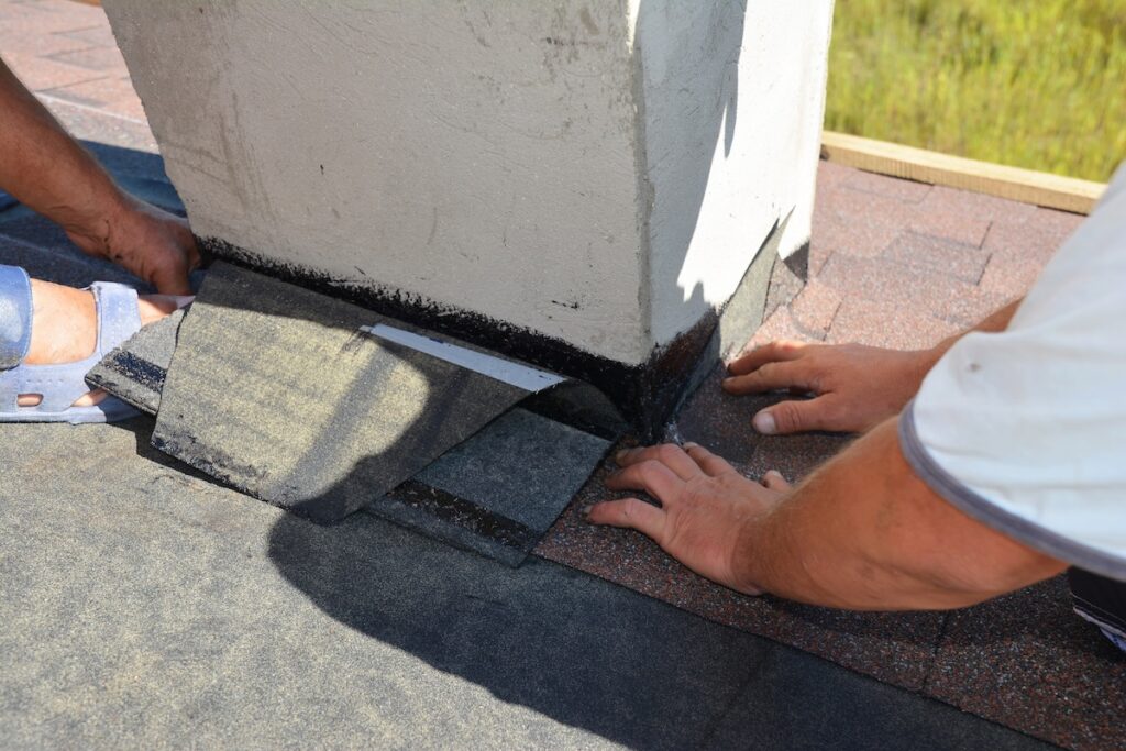 A close-up on a roofing construction, installation of asphalt shingles on roof sheathing around a house chimney using waterproofing corner flashing