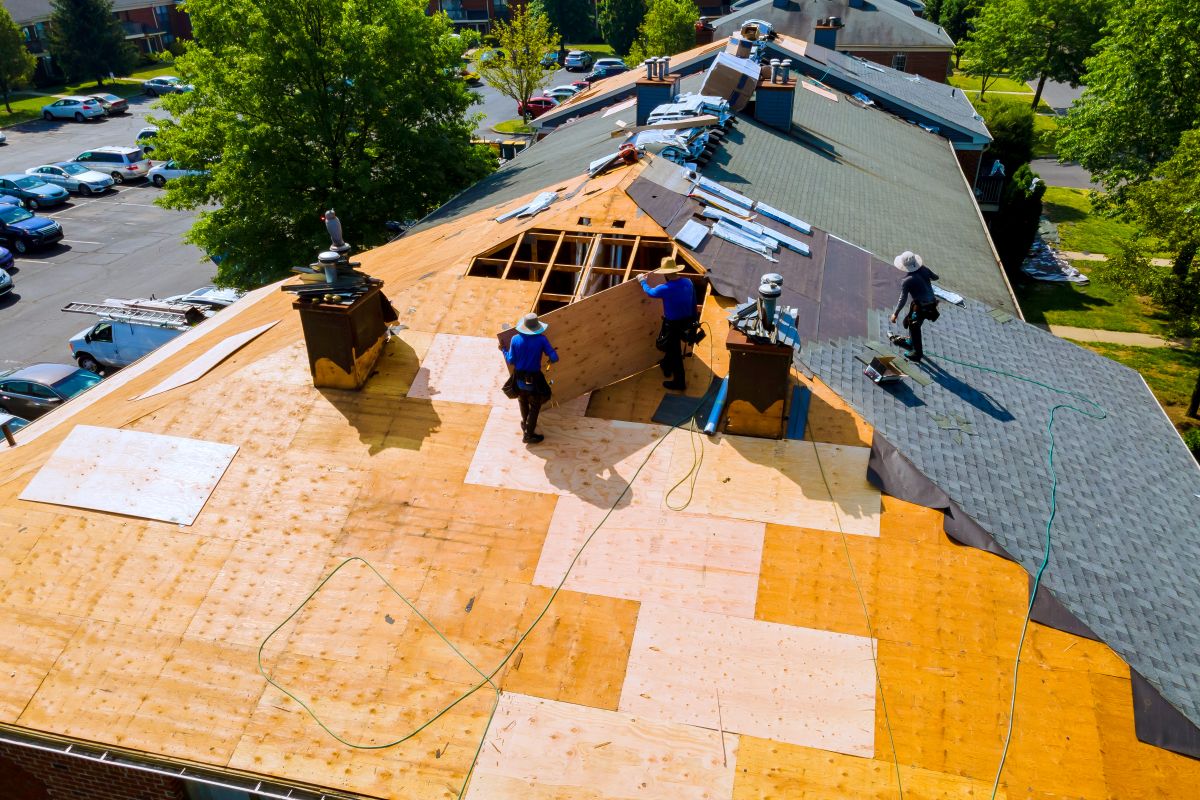 storm damage roof replacement workers replacing shingles on big house
