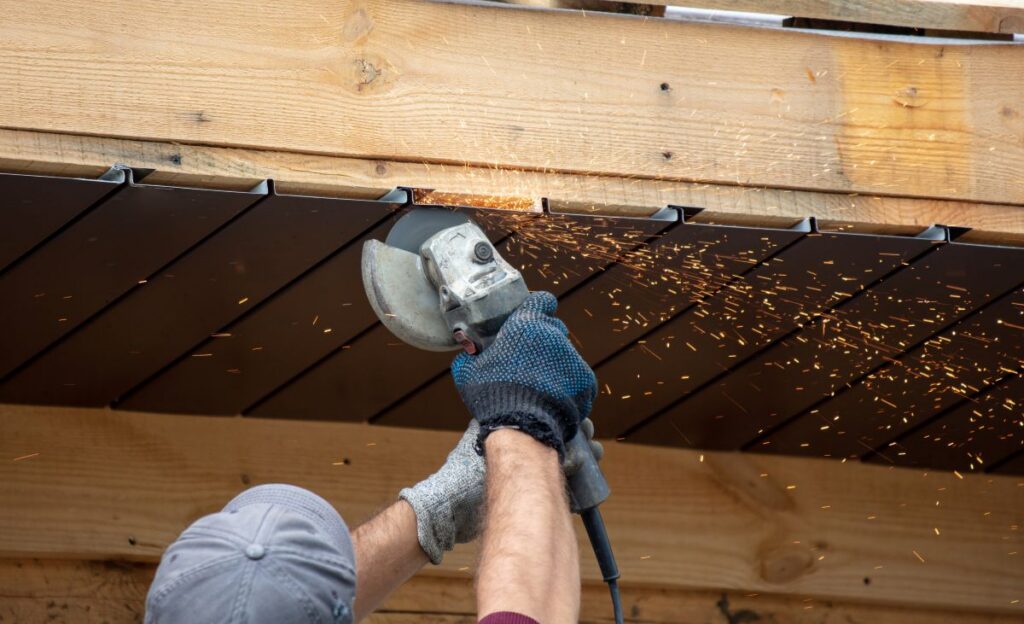 soffit repair worker using blue gloves and grey cap with electric saw repairing wooden roof 