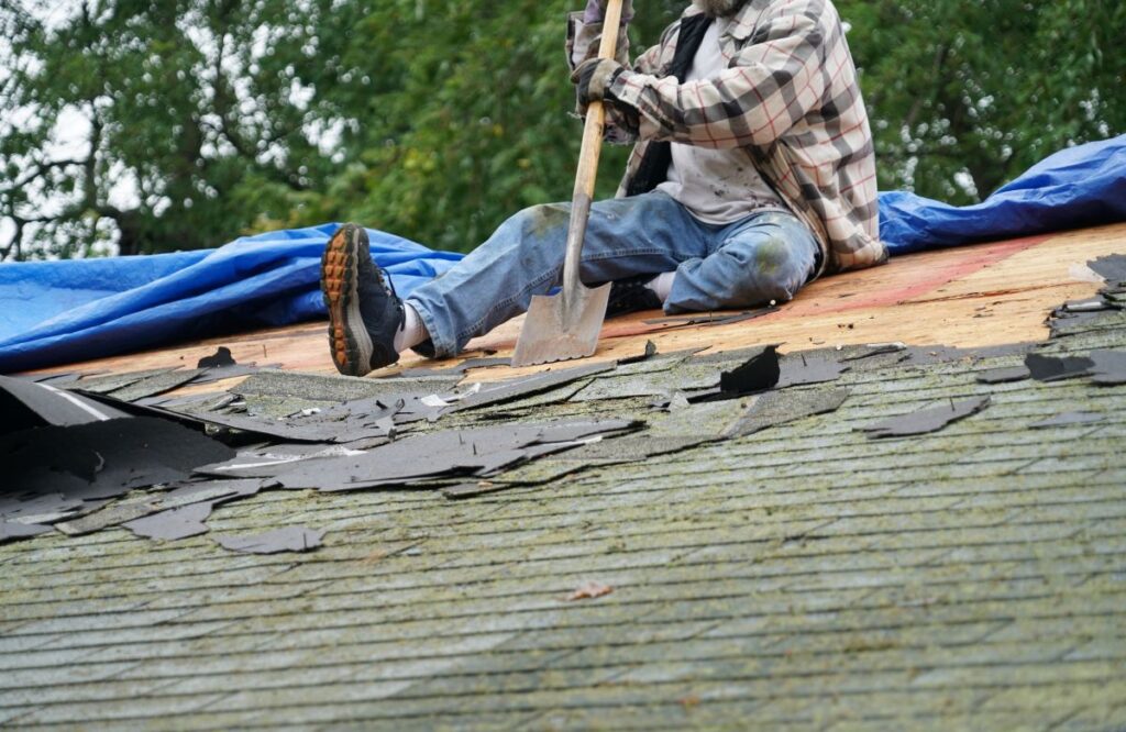 how much does a new roof cost worker removing old shingles using shovel on top of roof