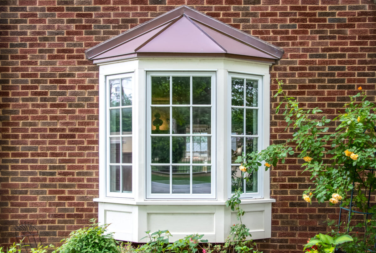 bay window installation Bay window with copper roof on traditional brick home with flowers below and yellow roses extending out onto the window in springtime