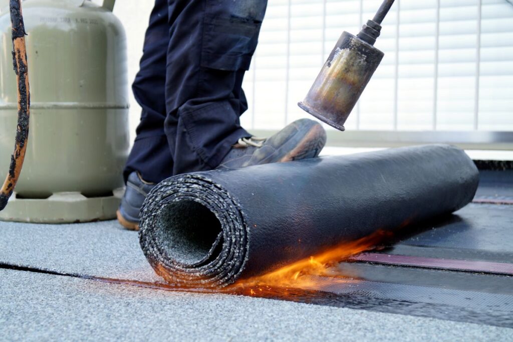 Flat roof installation with propane blowtorch during construction works with roofing felt. Heating and melting bitumen roofing felt. Roofing felt. Roofer working. 