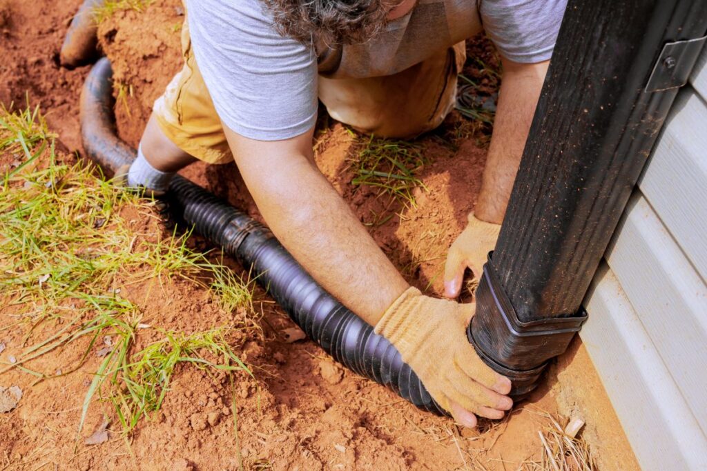 Man installing flexible gutter extension drainage pipe connector downspout with water draining down. Underground Gutter Drainage
