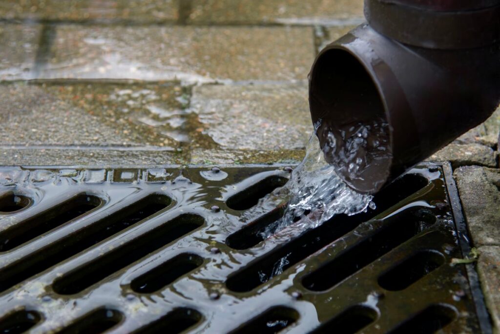 Rainwater drainage pipe flowing into metal grate outdoors
