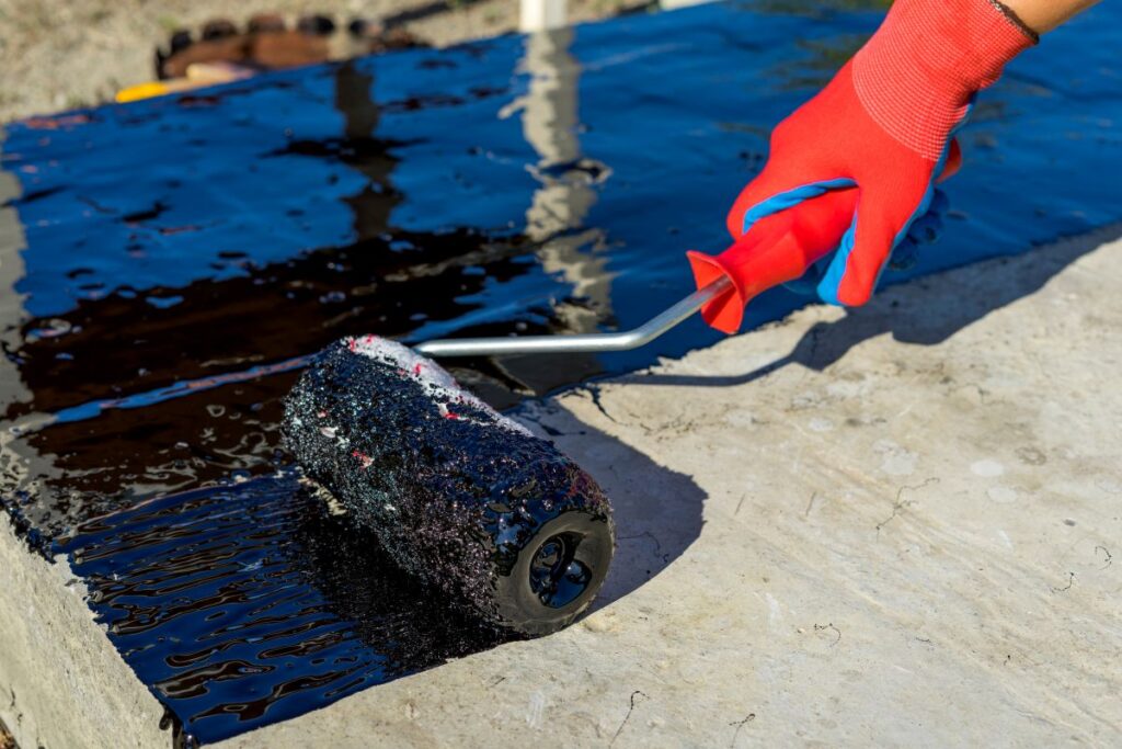 Workers hand in protective gloves applies bitumen mastic on the foundation.